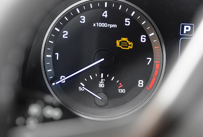 A tachometer in a car's dash showing a check engine light illuminated.