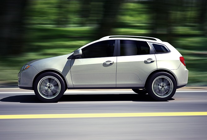 Side profile of a sedan driving on the road with the scenery in the background blurred to show that the car is moving.