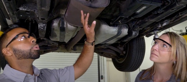 Auto technicians examining exhaust system under a vehicle lifted up at the shop